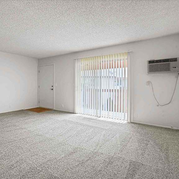a room with a carpeted floor, a window with blinds, and a door.