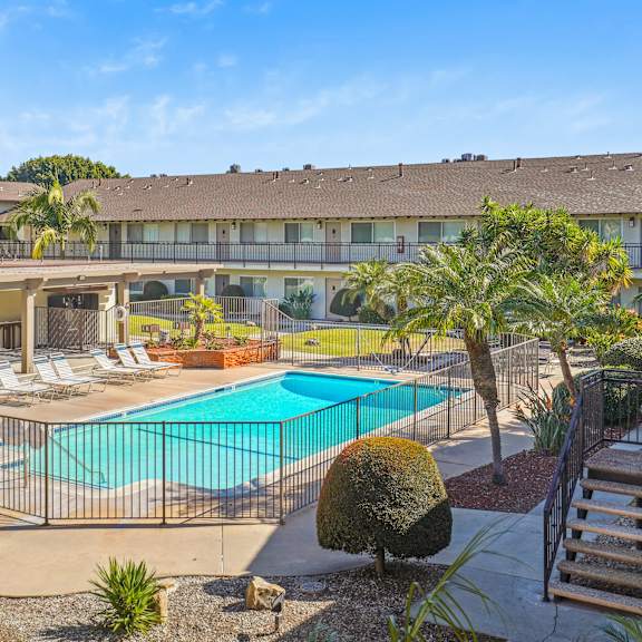 a large swimming pool is surrounded by a fence and palm trees.