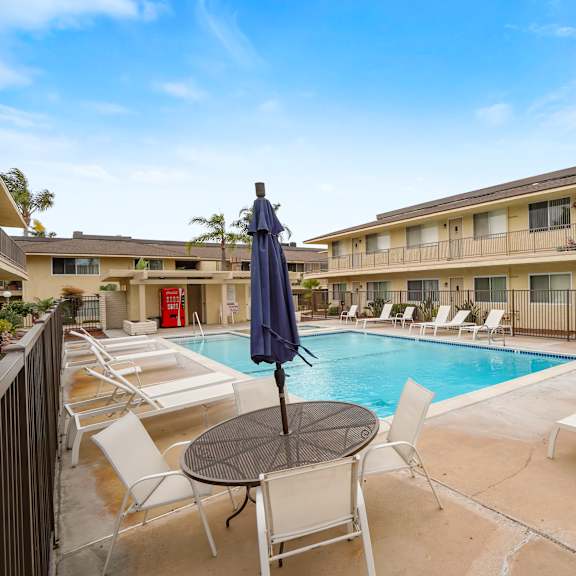 a pool area with chairs and a table with an umbrella.