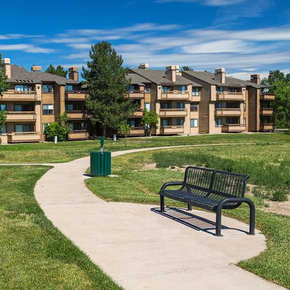 a park with a bench and a pathway leading to apartment buildings.