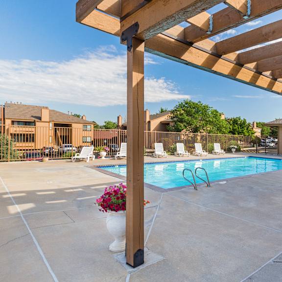 a pool area with a wooden pergola and a white chair.