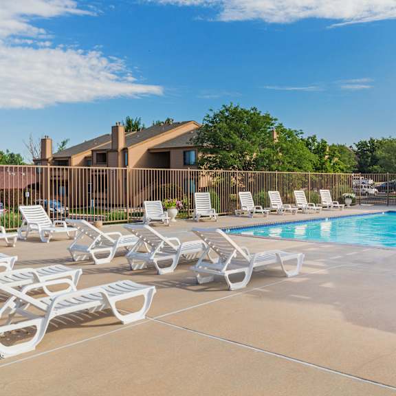 a pool area with sun loungers and a building in the background.