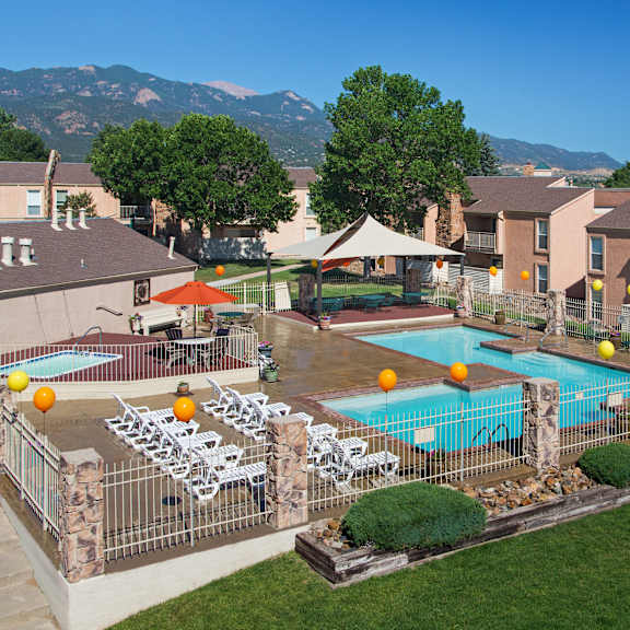 a pool surrounded by chairs and umbrellas with mountains in the background.