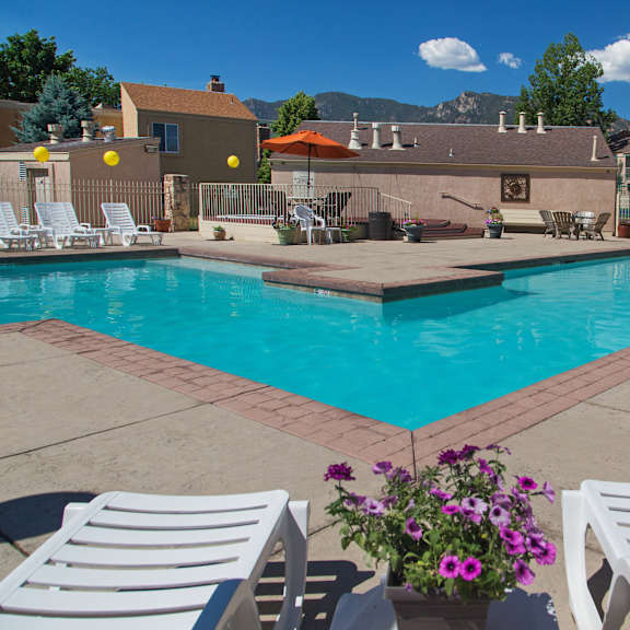 a pool surrounded by white chairs and a patio umbrella.