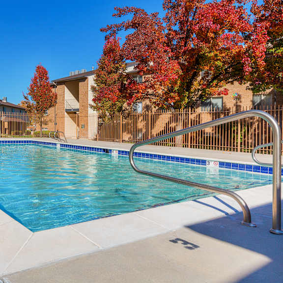 a swimming pool surrounded by a metal fence and trees with red leaves.