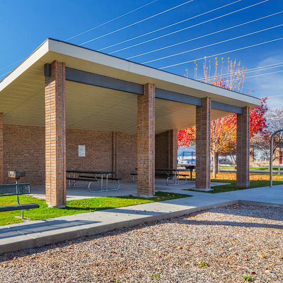 a covered picnic area with a bench in front of a brick building.