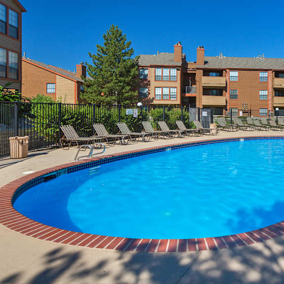 a swimming pool surrounded by chairs and trees in front of apartment buildings.