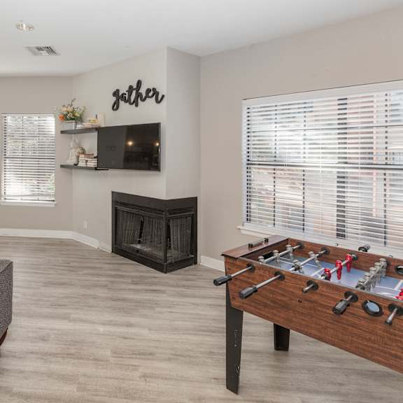 a living room with a grey couch, a foosball table, and a fireplace.