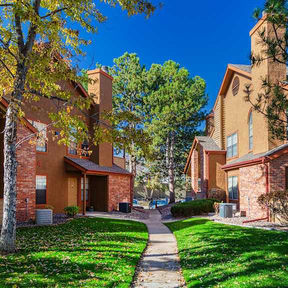 a row of houses with green lawns and trees in front.