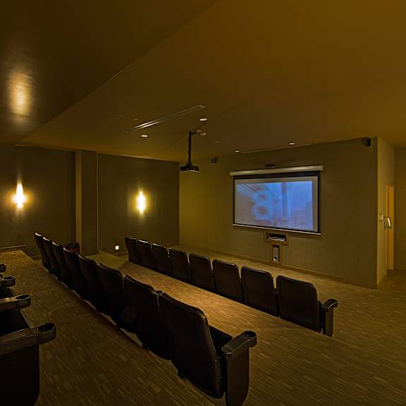 a dark room with a long table and chairs and a screen at the front.