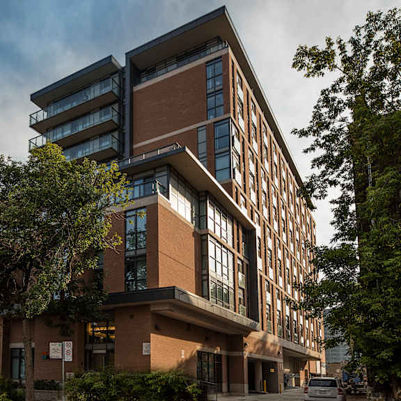 a modern building with a mix of brown and beige colors, surrounded by trees and a cloudy sky.
