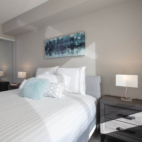 a bedroom with a large bed, a nightstand with a lamp, and a painting on the wall.