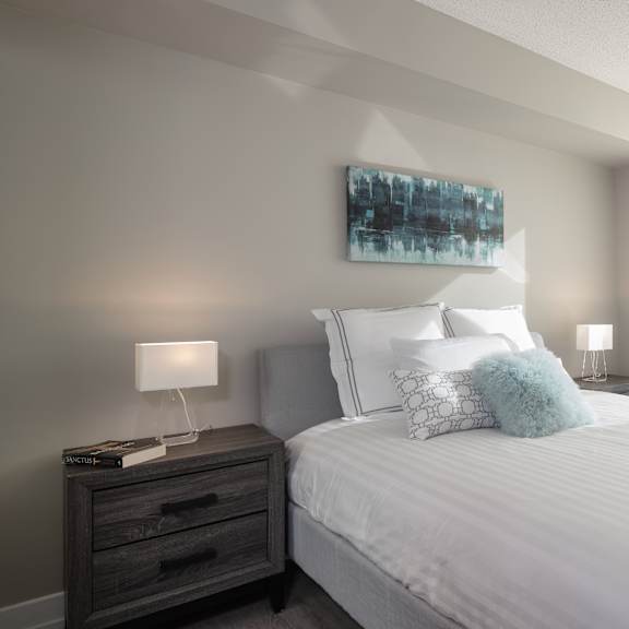 a bedroom with a white bed, a nightstand with a lamp, and a painting on the wall.