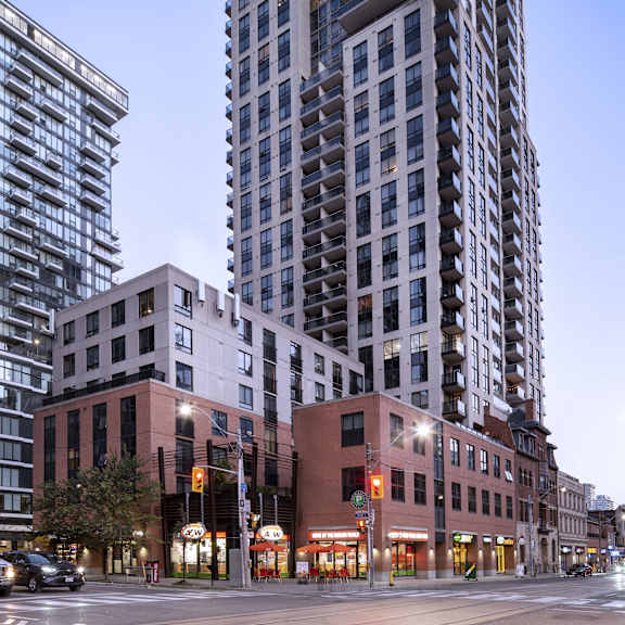 a tall building with many windows stands in front of a row of smaller buildings.