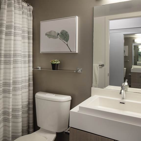 a bathroom with a toilet, sink, and a painting of a plant.