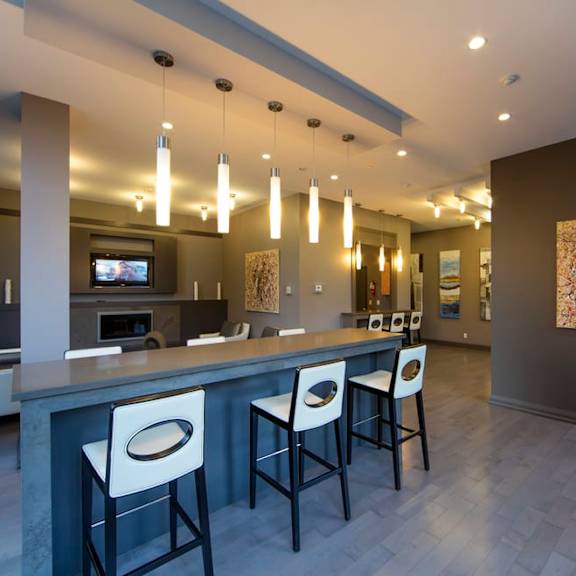 a bar with white chairs and a gray countertop in front of a living room with a