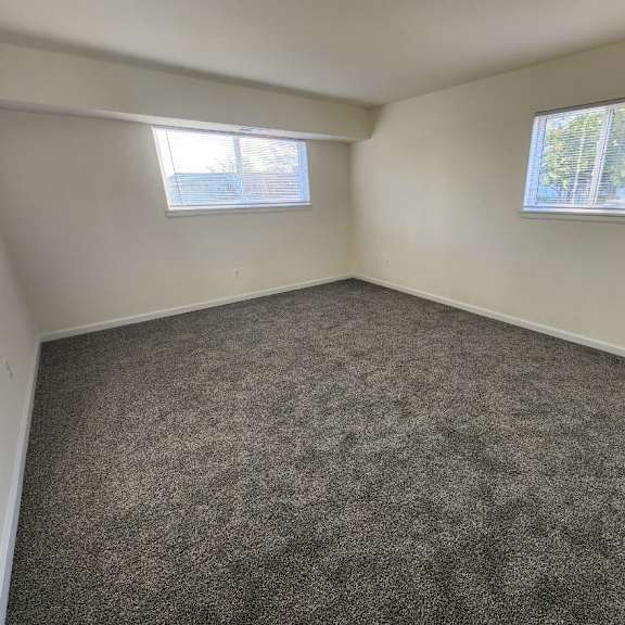 a room with grey carpet and two windows.