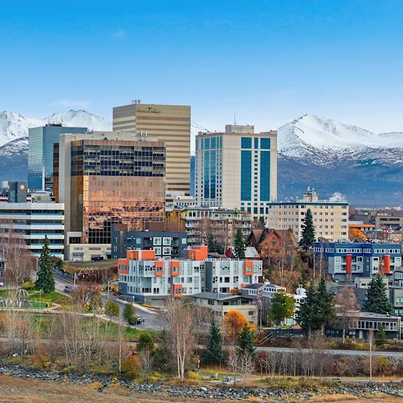 a cityscape with buildings and snow-capped mountains in the background.