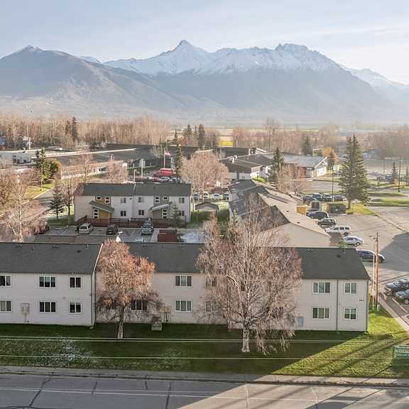 a large white building sits in the middle of a parking lot with mountains in the background.