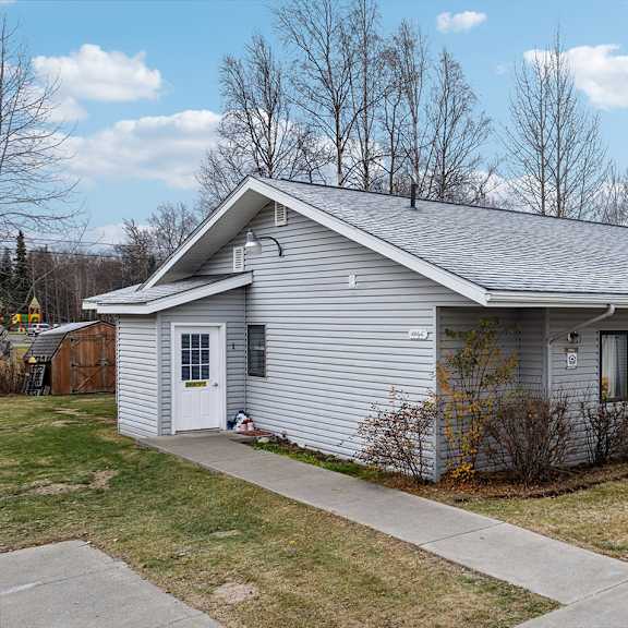 a house with a grey roof and a white door is surrounded by a grassy area.