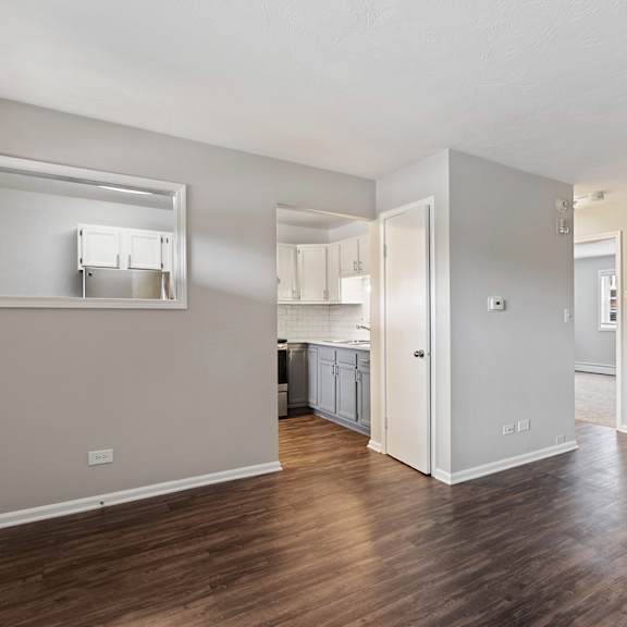 a bedroom with a medium hardwood floor and a kitchen in the background at the hinsdale, hinsdale