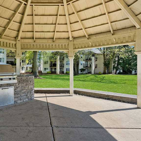 a gazebo with a stone pillar and a metal door is surrounded by a concrete floor and a wooden roof.