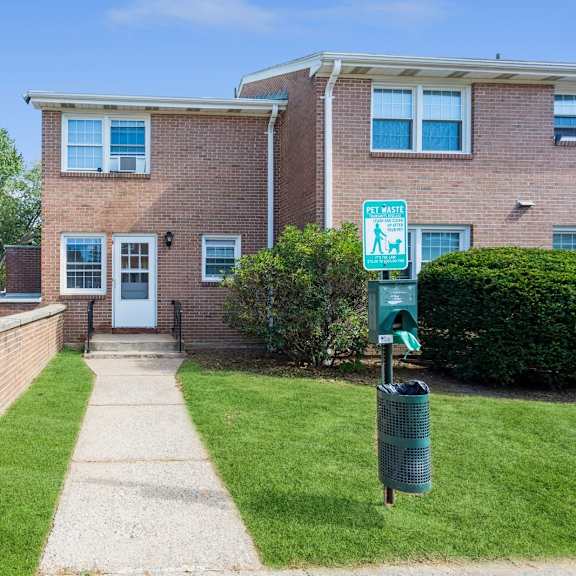the front of a brick apartment with a sidewalk and a doggy trash station
