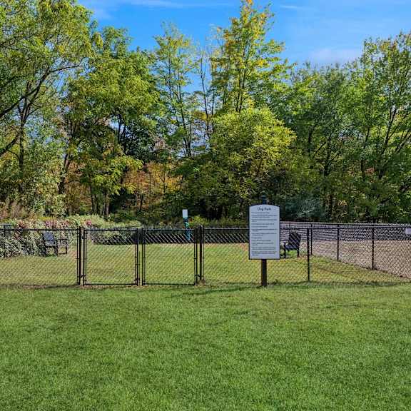 a dog park with a fence and a sign in the grass with the rules at arbor commons