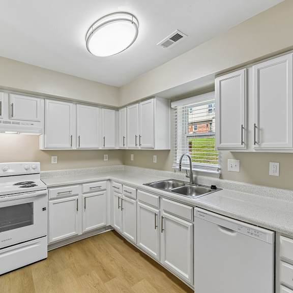a white kitchen with a stove, sink, and cabinets.