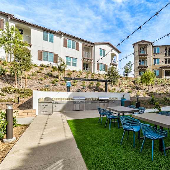 a patio with blue chairs and a table is in front of apartment buildings.