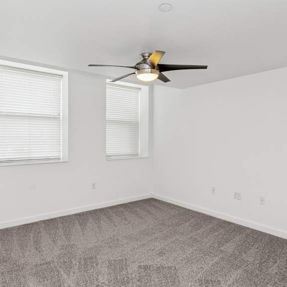 a room with a ceiling fan and two windows.