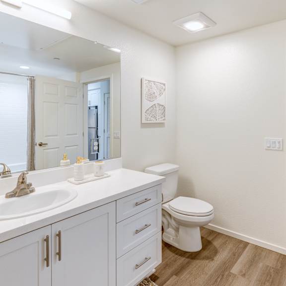 a white bathroom with a toilet, sink, and mirror.