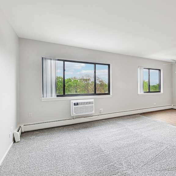 a spacious room with a grey carpet and kitchen in the background