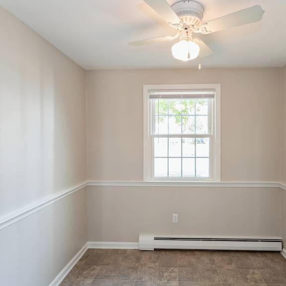 empty carpeted room with ceiling fan and window
