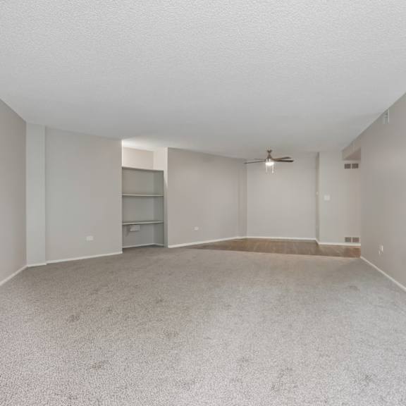 a spacious empty room with a carpeted floor and a ceiling fan.