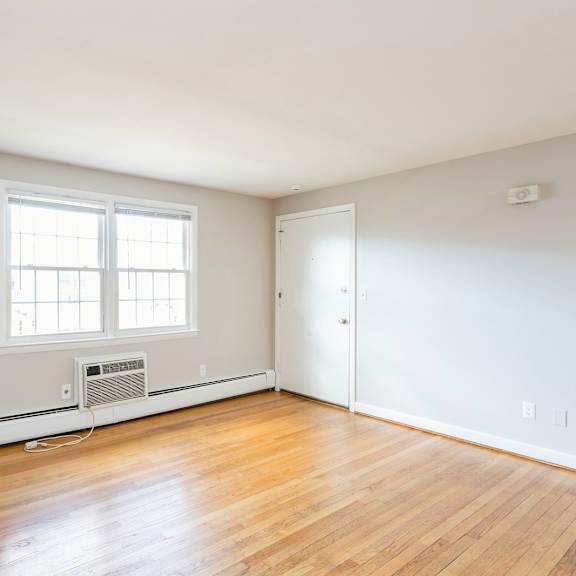 an empty room with wood floors, a white wall, and window