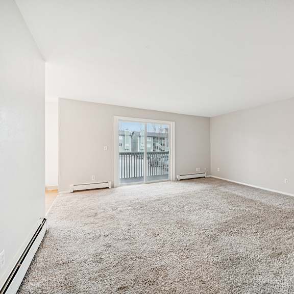 a spacious room with a carpeted floor and a view of a balcony through a window.
