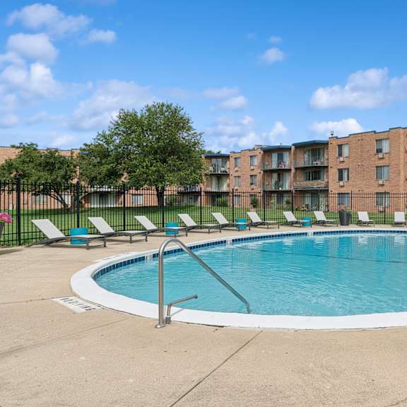 a swimming pool surrounded by lounge chairs and trees in front of a brick apartment building.