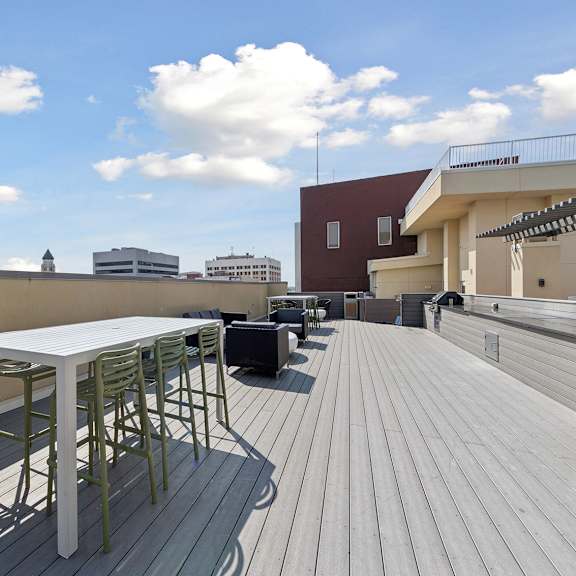 a table and chairs are on a wooden deck with buildings in the background.