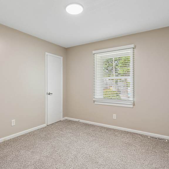 a room with a carpeted floor, a window with blinds, and a door.