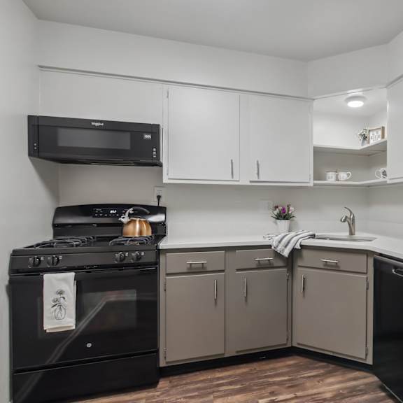 a black refrigerator is on the right side of a kitchen with white cabinets and a black stove.