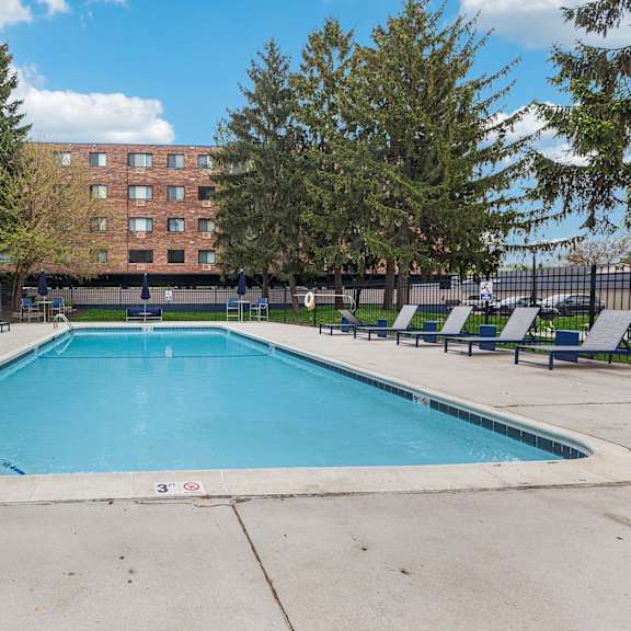 a swimming pool in front of a brick building with trees around.
