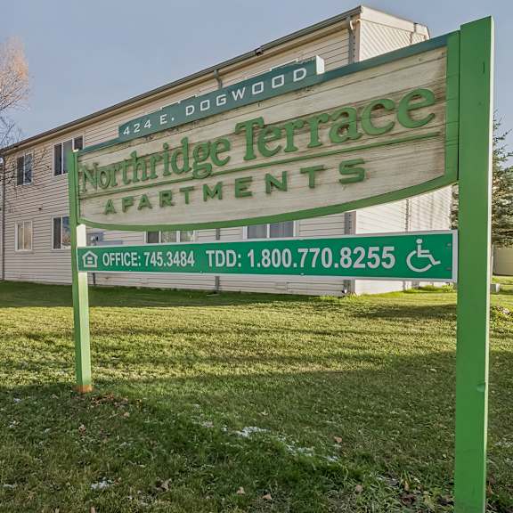 a green sign for nookridge terrace apartments sits in front of a building.