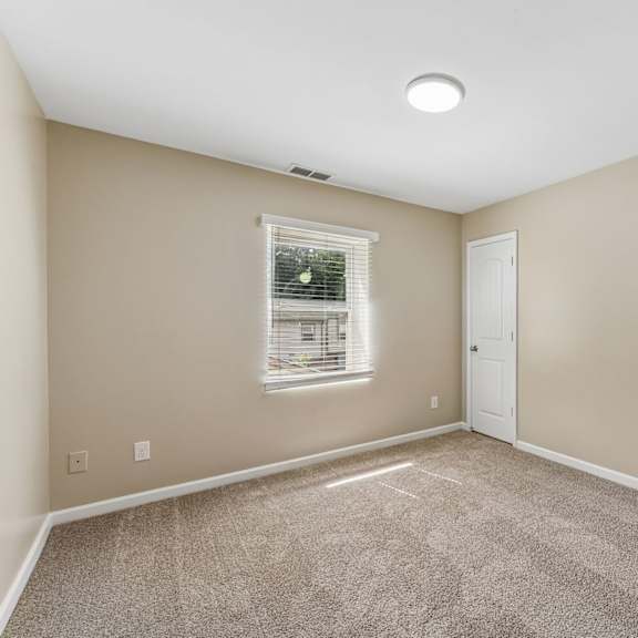 a room with a carpeted floor, a window with blinds, and a white door.