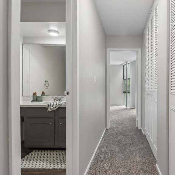 a long hallway with white walls and a bathroom visible in the distance.