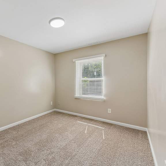 a room with a carpeted floor and a window with blinds.