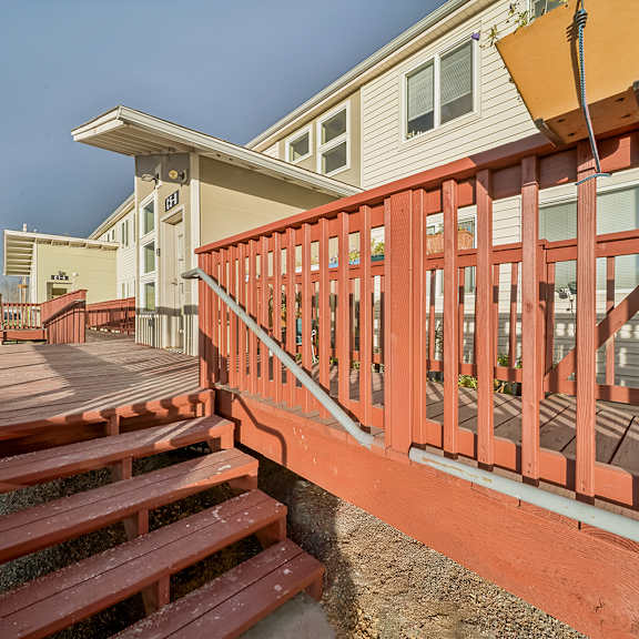 a wooden deck with a red railing and steps leading to a house.