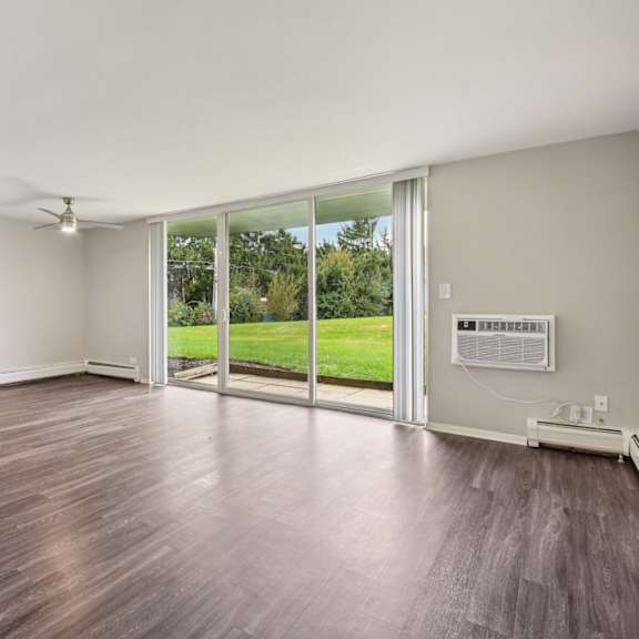 a room with wooden floors and sliding glass doors leading to a green outdoor area.