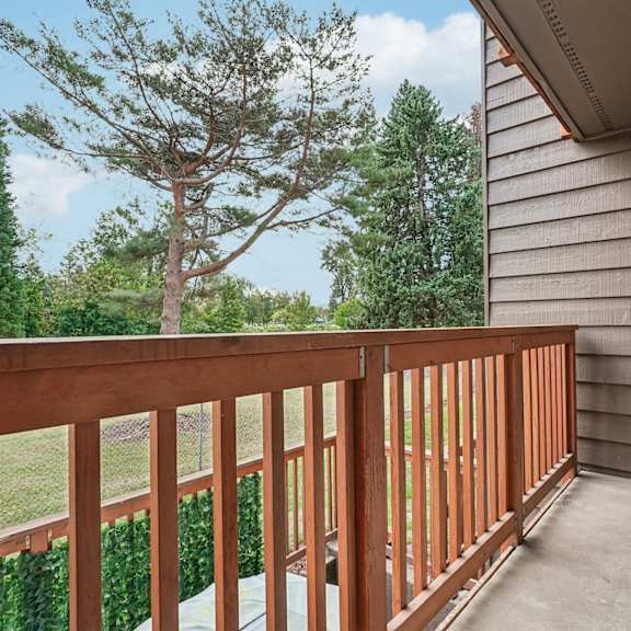 a wooden balcony with a railing overlooking a green tree.