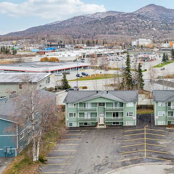 a parking lot with two green buildings in the foreground and mountains in the background.